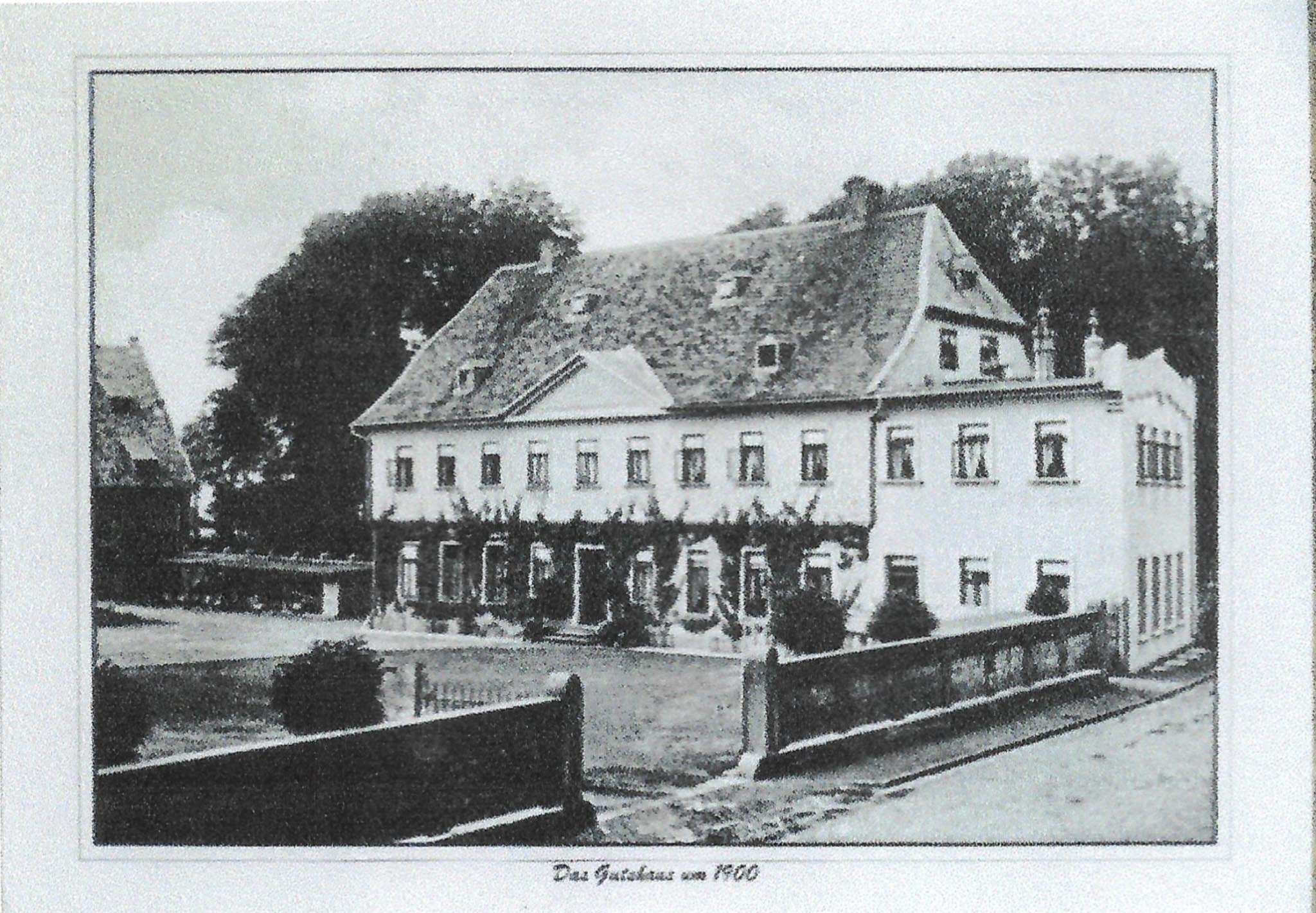 Historische Schwarz-Weiß-Fotografie des Gutshauses in Heißum um 1900, zweistöckiges Fachwerkgebäude mit Walmdach, Bäumen und Zaun davor.